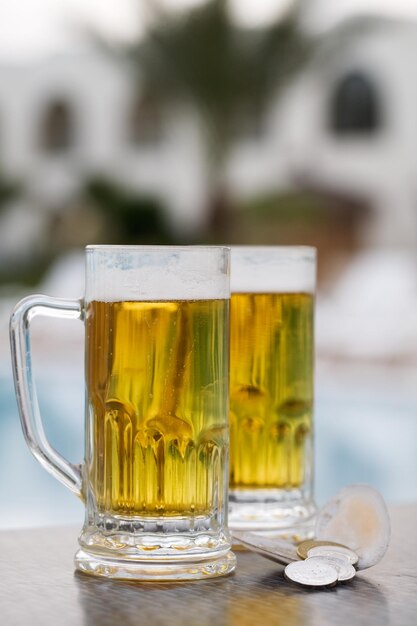 Two beer mugs and currency by swimming pool in tropical resort