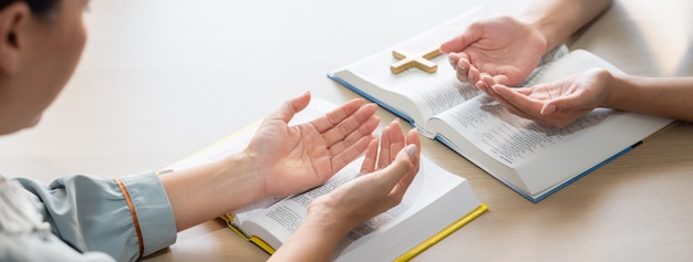 Two believer praying together on holy bible book faithfully with wooden cross placed at wooden church Concept of hope religion faith christianity and god blessing Facing hand Burgeoning