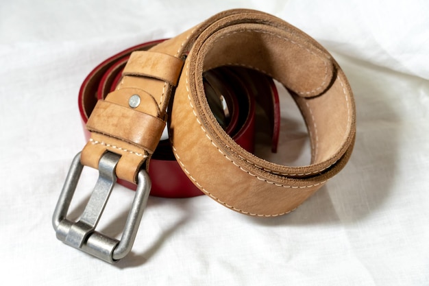 Two belts made of thick genuine leather on a white background made of linen fabric Production of handmade belts from natural environmentally friendly materials