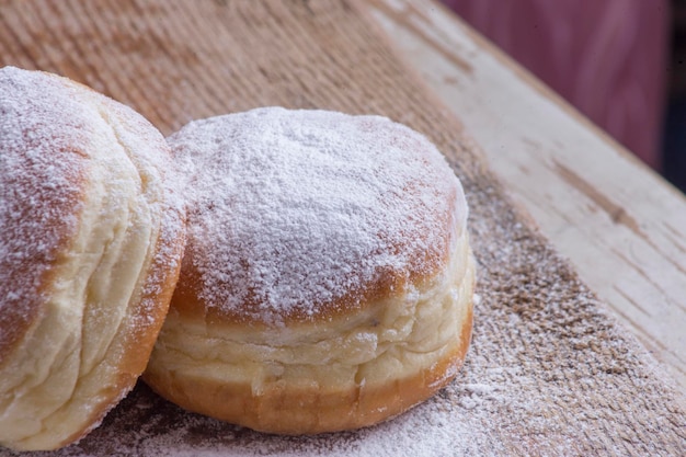 Two Berliner donuts sprinkled with icing sugar on a wooden background.