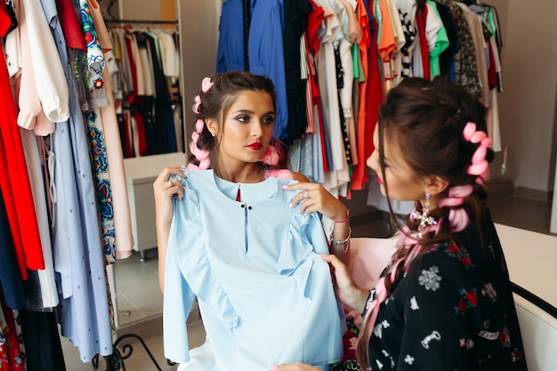 Two best girlfriends on shopping, making choose and looking at blue dress.