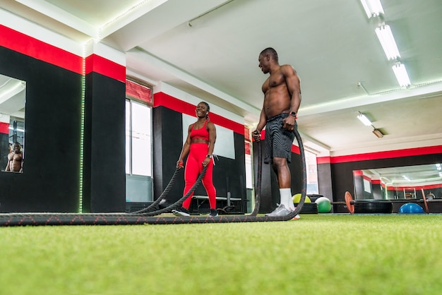 Two black bodybuilder athletes in a sports gym tired of pes from performing a rope aerobic exercise to strengthen arms and chest. Concept of strengthening the body in gym