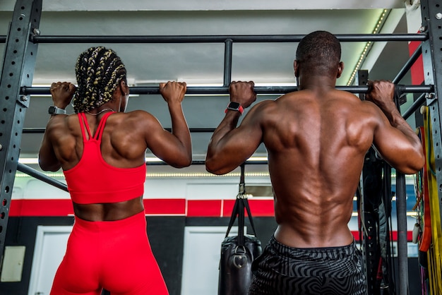 Two black bodybuilders athletes in a sports gym doing a barbell back exercise . Concept of strengthening the body in gym