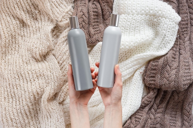 Two blank plastic bottles in woman hands on colored knitted texture background top view choice conce