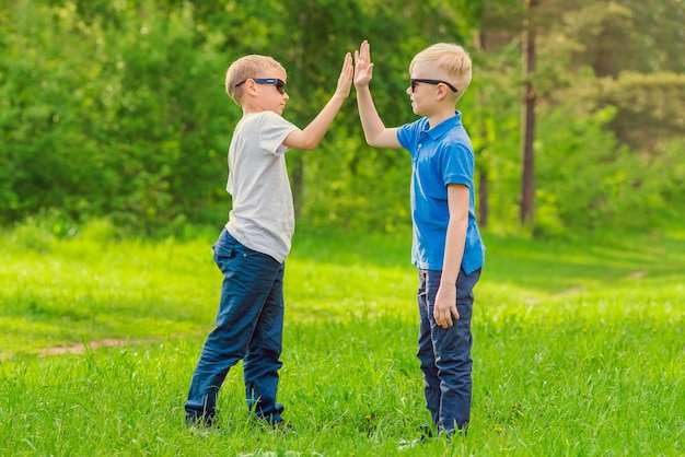 Two blond boys in sunglasses give five their hands in the summer park Toned