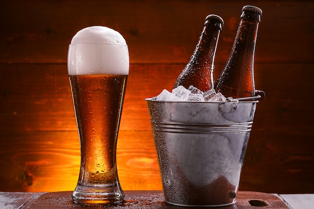 two bottles of beer in a bucket with ice and a glass of beer with lush foam