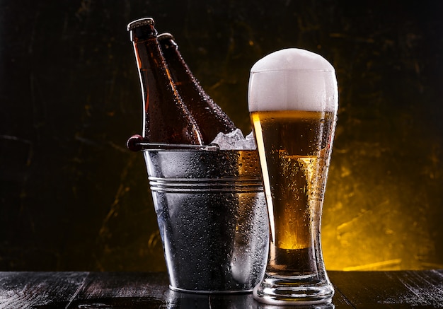 two bottles of beer in a bucket with ice and a glass of beer with lush foam