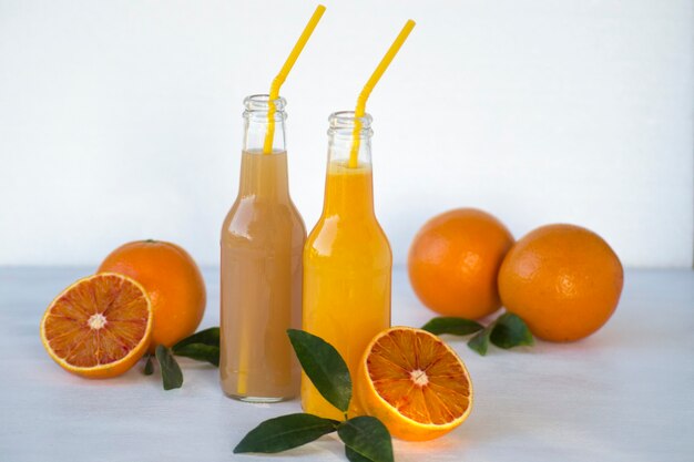 Two bottles of citrus juice and fresh orange fruits on white background Copy space