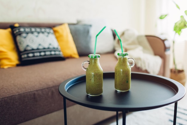 Two bottles of green fruity smoothie on living room table drinking healthy detox beverage at home