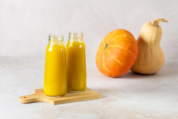 Two Bottles of Pumpkin Juice on Wooden Cutting Board Raw Whole Pumpkin Autumn Healthy Diet Drink