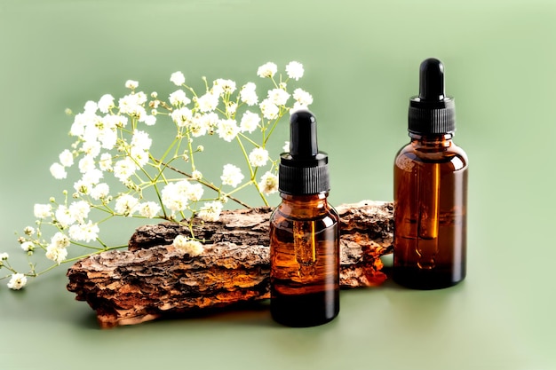 Two bottles with a dropper with a serum for skin care of the face against the background of the bark of the tree and flowers