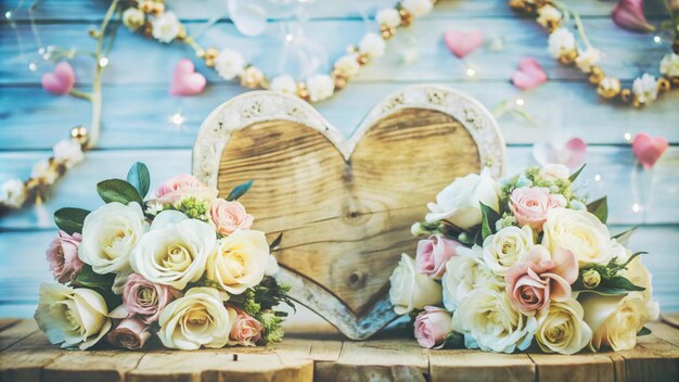 Two bouquets of white and pink roses with a wooden heart and heartshaped decorations on a blue wood background