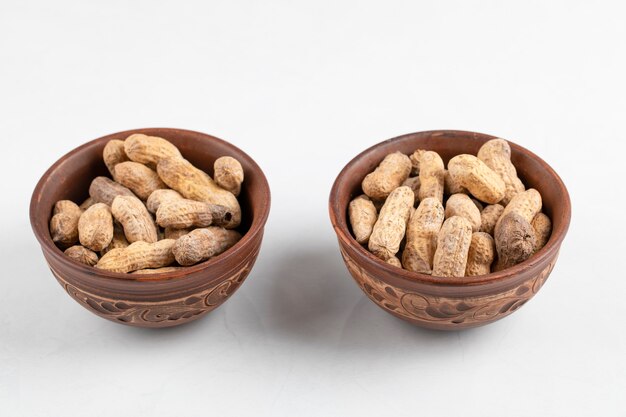 Two bowls of fresh peanuts in shell isolated on white surface.