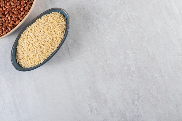 Two bowls full of raw rice and beans on stone background. 