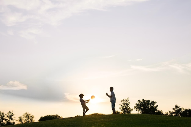 Two boys are playing with a ball on sunset.