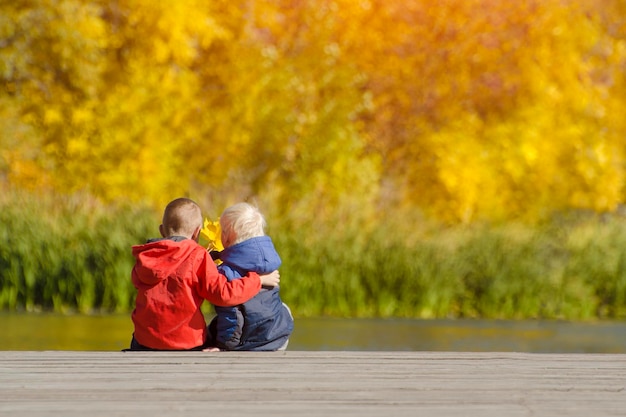 Two boys are sitting on the pier Autumn Back view