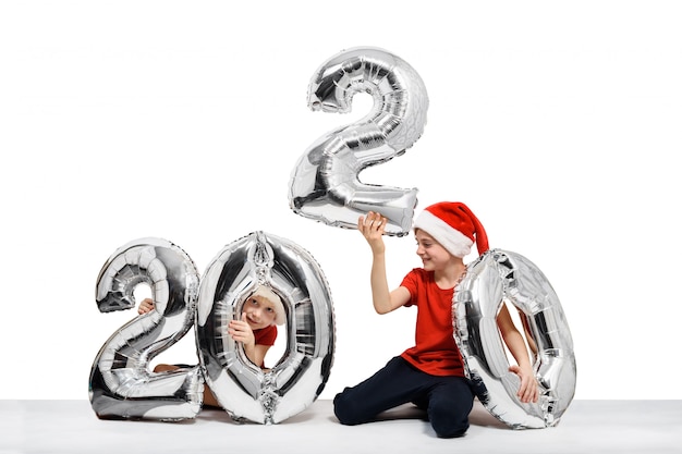 Two boys in Christmas hats are holding silver balloons