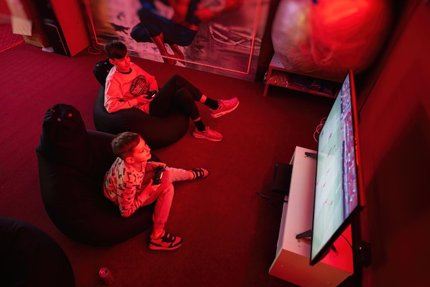 Two boys gamers play football gamepad video game console in red gaming room