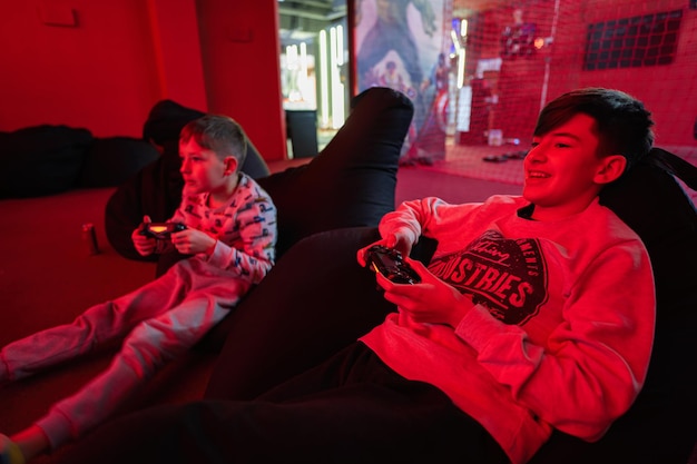 Two boys gamers play gamepad video game console in red gaming room