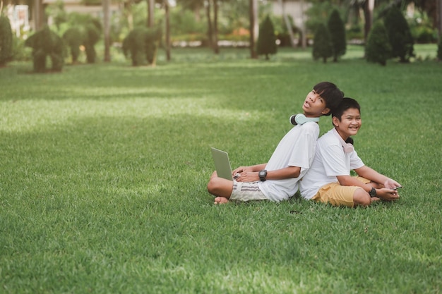 Two boys sit in their garden. Children happily play computer games.