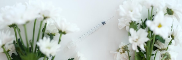 Two branches of white chrysanthemums in middle of syringe with needle