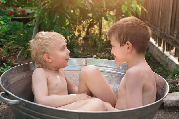 Two brother are playing outside in a basin with water on sunny summer day Weekend in country