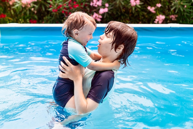 Two brothers of different age are playing in a swimming pool in summer during vacation