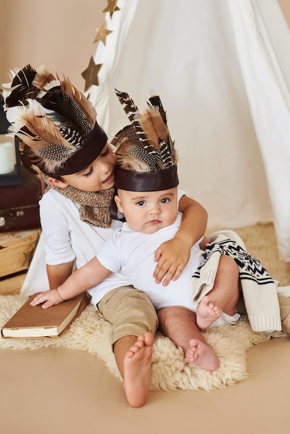 Two brothers playing indian in tent on beige background