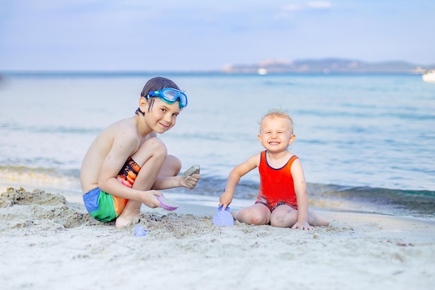 Two brothers playing on a sand at the seaside. Beach activities for children outdoords in summer. Happy family vacation concept, copy spoace.