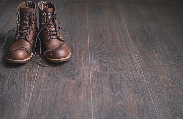 Two brown work leather men boots with untied laces on a wooden floor