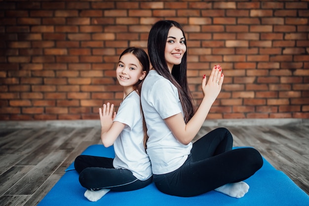 Two  brunette and fit sisters sitting back to back at gym and practicing yoga.