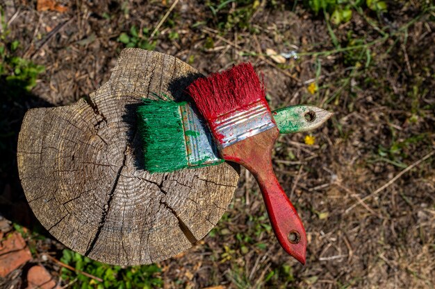 Two brushes with green and red paint on a wooden deck