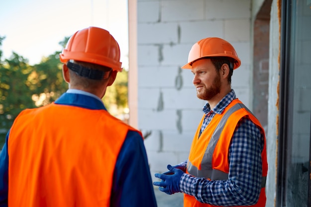 Two builder workers standing and talking at construction site of unfinished home apartment