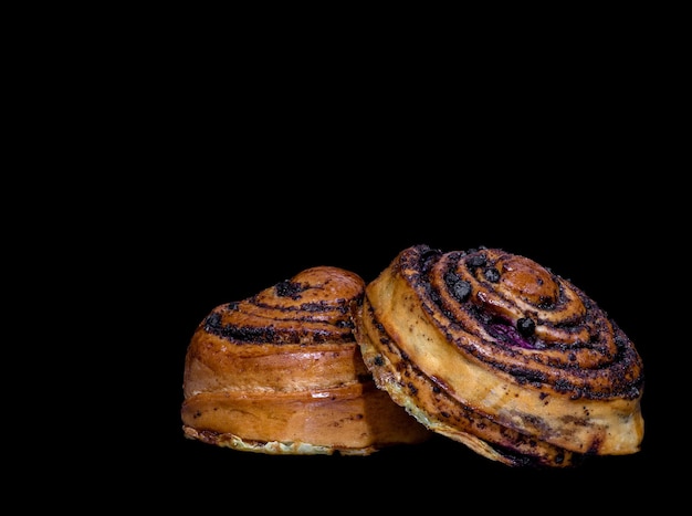 Two buns with poppy seeds cinnamon and cherries on a black background