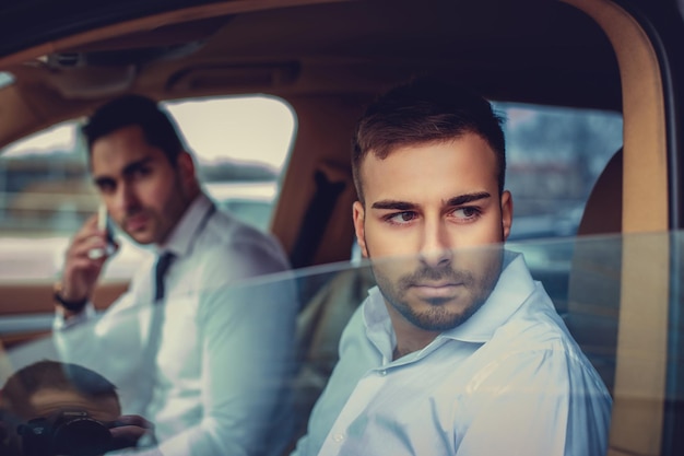 Two business men in a white shirts in a car.