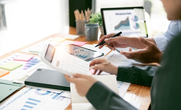 Two business people point to graphs and charts on tablet to analyze data balance sheet account and net profit to plan new sales strategies