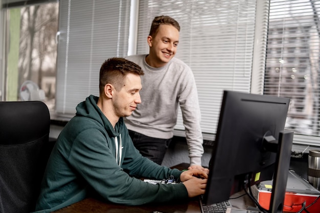 Two business people and software developers working as a team in office. Boys looking at the computer screen and smiling