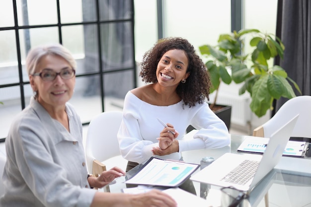 Two business women smile while working together on a laptop at a table in the boardroom in the office