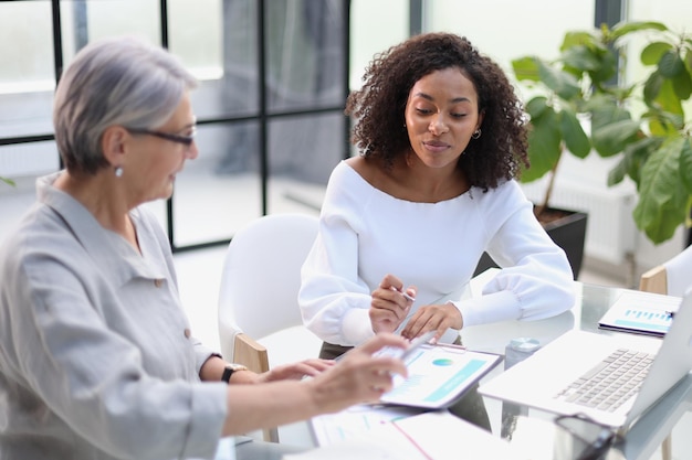 Two business women smile while working together on a laptop at a table in the boardroom in the office