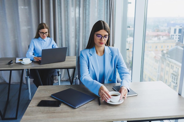 Two business women at work Smart employee in glasses successful freelancer in a jacket workflow in an office with large windows