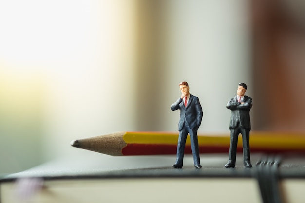 Photo two businessman miniature figures standing on black notebook with pencil.