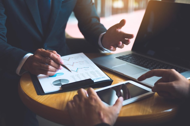 Two businessmen are discussing and analyzing the performance of the company business paper and looking for numerical data via tablets