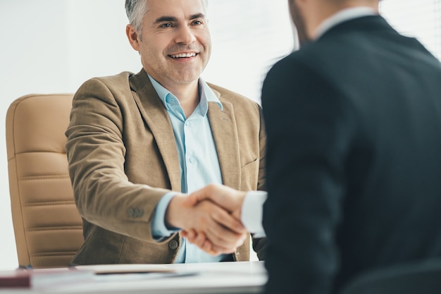 The two businessmen handshaking near the desk