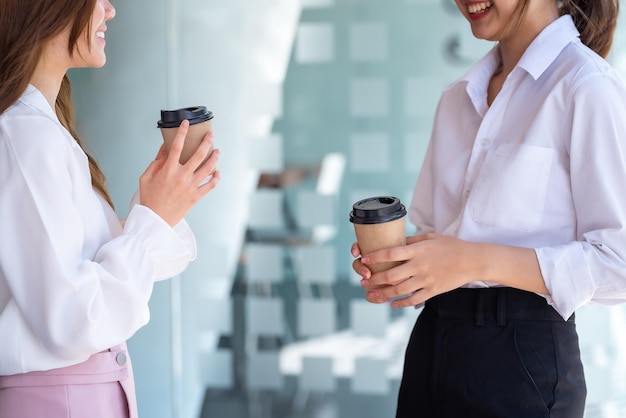 Two businesswoman standing and talking holding coffee in the office