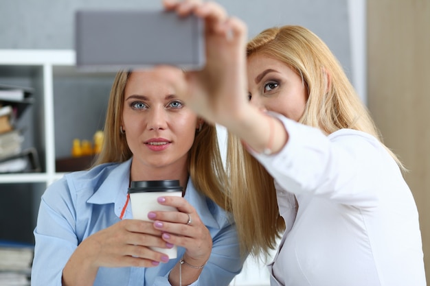 Photo two businesswomen in the office smile and do selfie