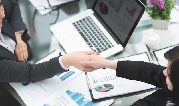 Two businesswomen shaking hands over a desk as they close a deal