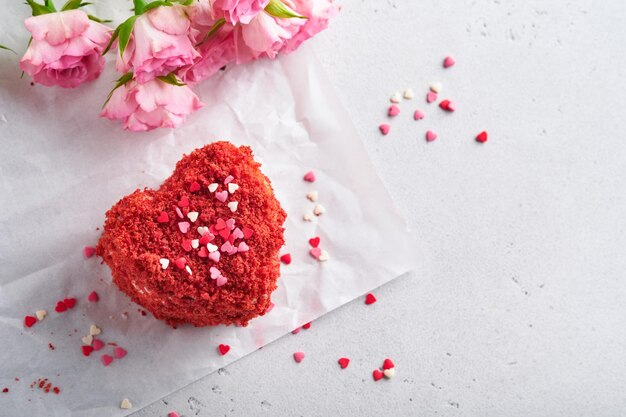 Two cakes Red velvet in shape of hearts on white plate rose flowers and cup of coffeeon on pink romantic background Dessert idea for Valentines Day Mothers or Womens Day Tasty homemade dessert