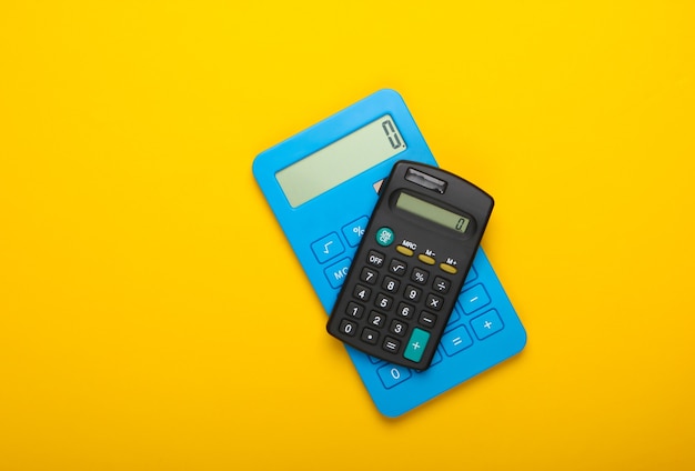 Two calculators on yellow background. Top view.