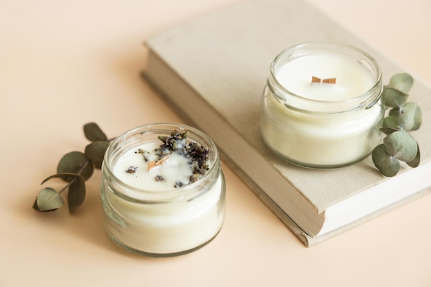 Two candmade candles from paraffin and soy wax in glass with wooden wick and dry herbal isolated on pastel beige background Flat lay top view copy space