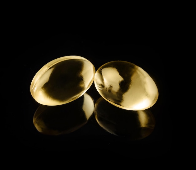 Two capsules of vitamin D3 closeup on a black background